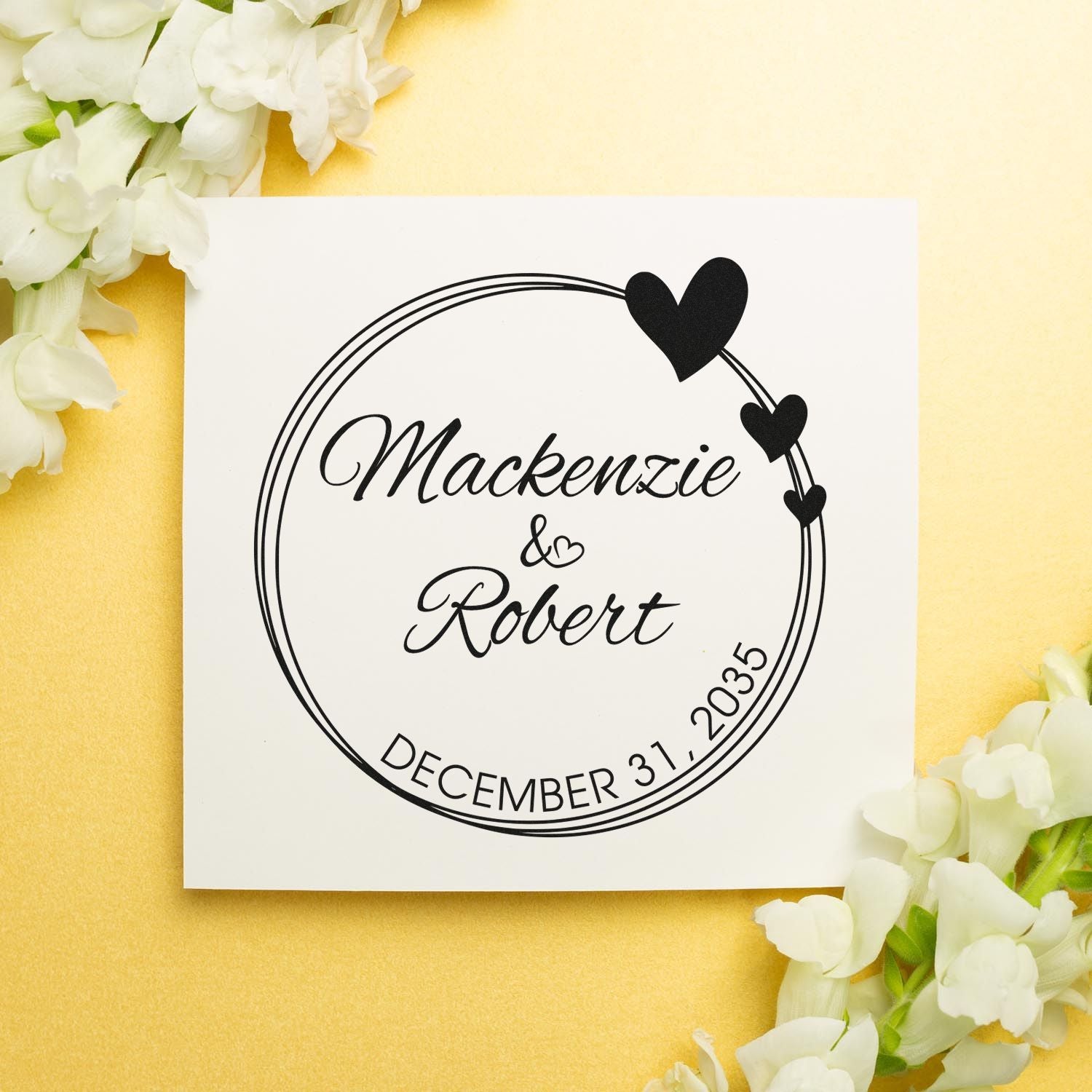 Custom black wedding stamp seal with hearts, Mackenzie & Robert, December 31, 2035, on a white card with gold background and white flowers.