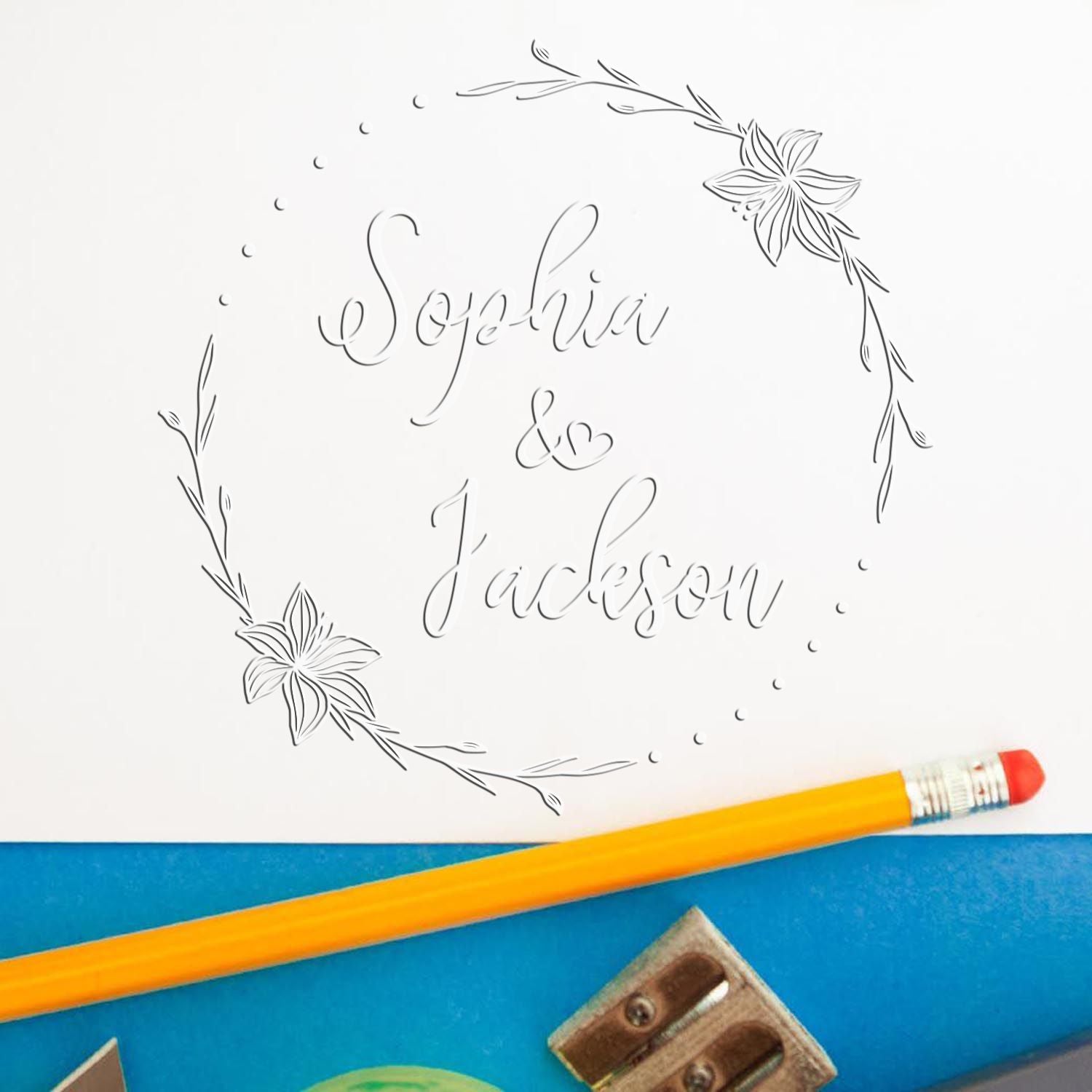 Custom floral stamp and seal design reading Sophia & Jackson in gray line art on white paper, with a yellow pencil.