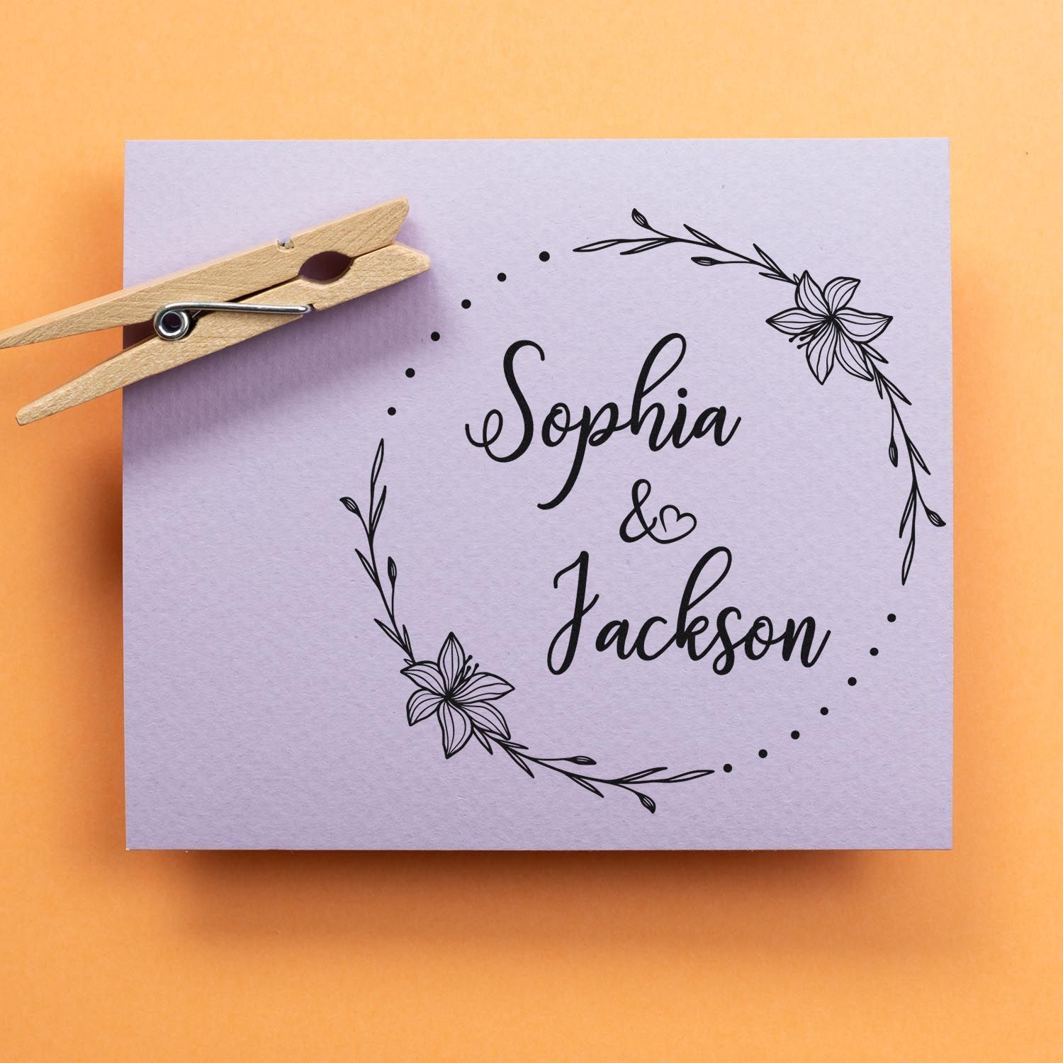 Custom wooden stamp seal with lavender card, black floral wreath, and Sophia & Jackson names on orange background.