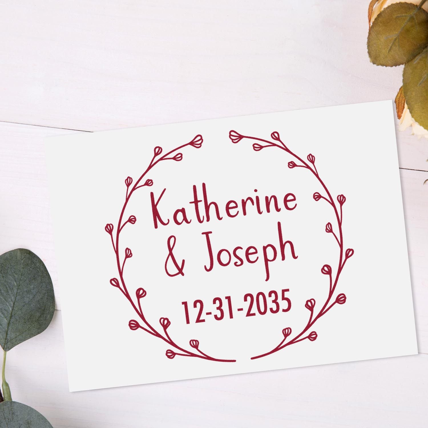Burgundy custom wedding stamp seal with floral wreath, Katherine & Joseph, and 12-31-2035 on a white card.