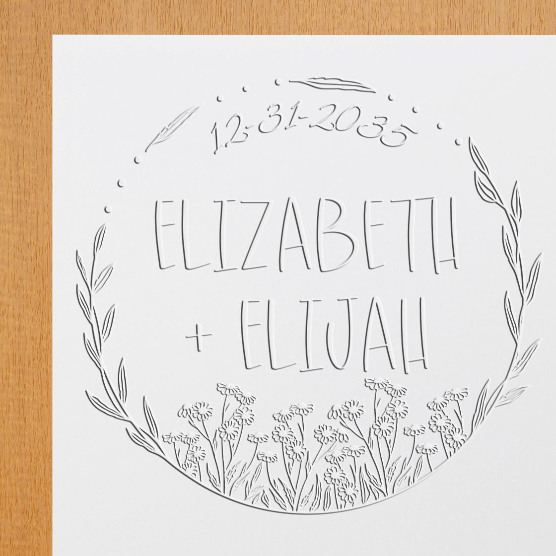 White embossed wedding stamp seal with floral wreath, Elizabeth + Elijah, and date 12-31-2023 on a white card.