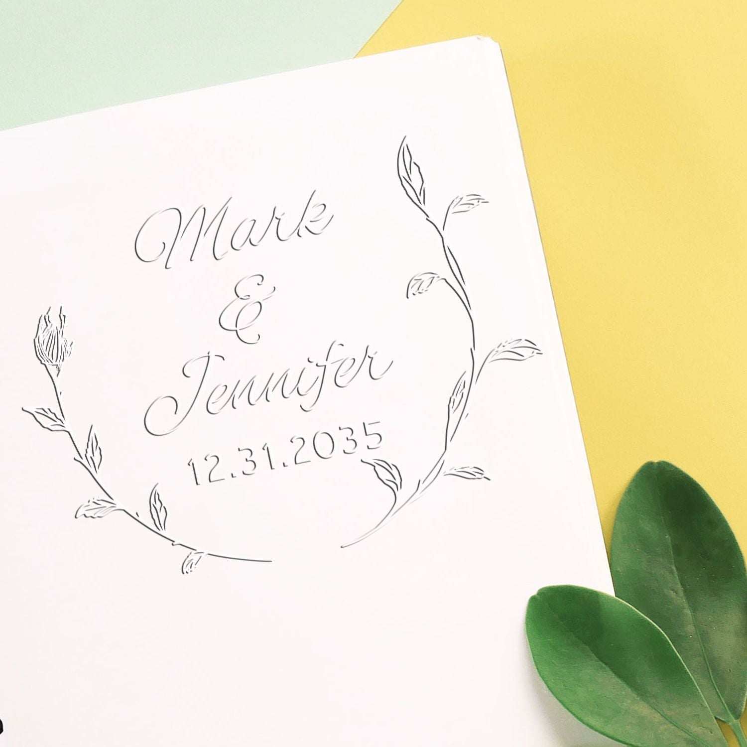 Custom botanical wedding stamp seal on white card, gray script for Mark & Jennifer, date 12.31.2035, yellow background, green leaves.