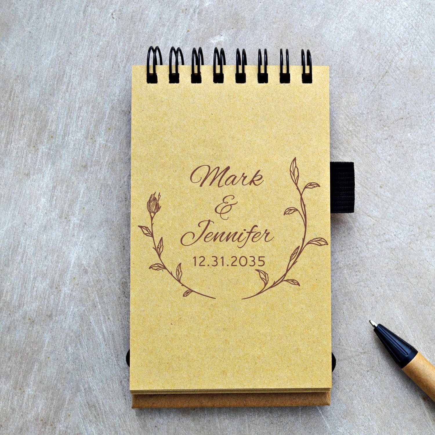Custom stamp and seal on a gold spiral notepad with brown floral wreath, Mark & Jennifer and date 12.31.2035.