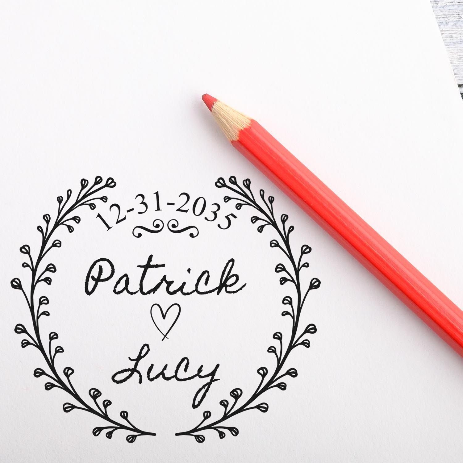 Red pencil on white paper beside a black custom stamp and seal with leafy wreath, 12-31-2035, Patrick and Lucy.