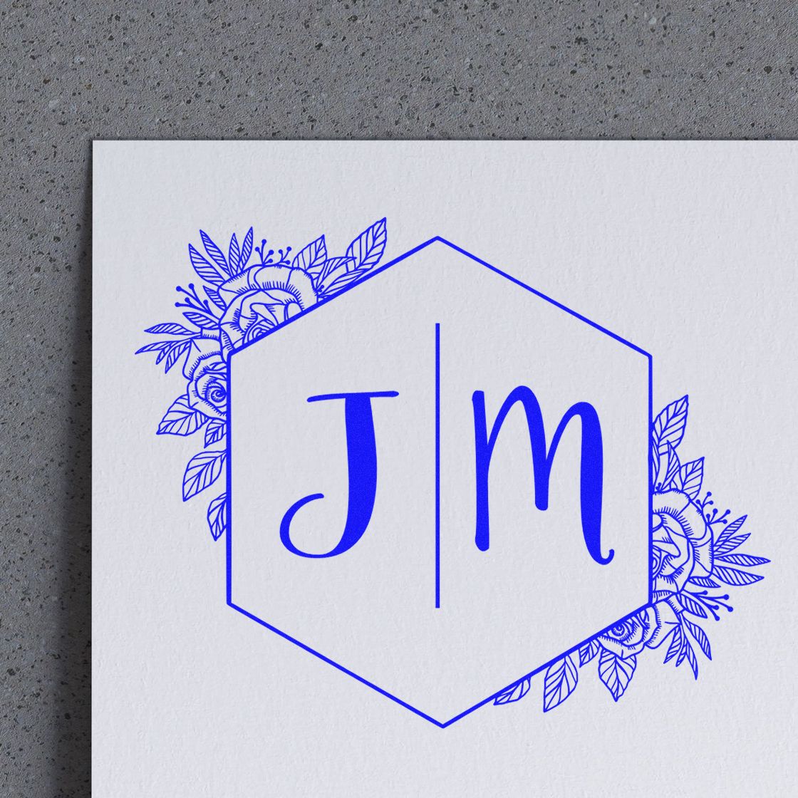 Blue monogram stamp seal with J and M inside a hexagon, accented by floral leaves on white paper.