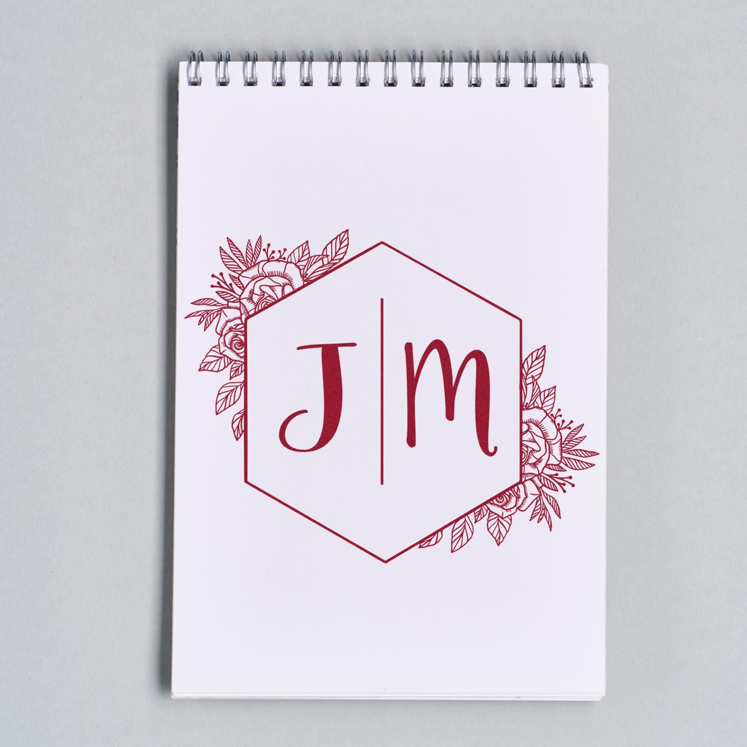 Maroon custom stamp and seal with J|m monogram in a hexagon floral border on a white spiral notebook.