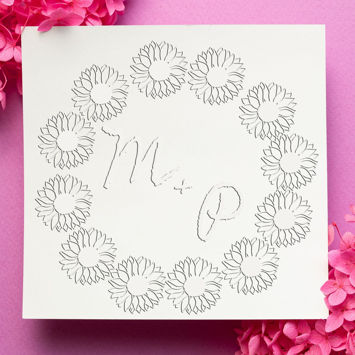 White stamp and seal card with floral wreath embossing and faint logo, on bright pink background with pink blossoms.
