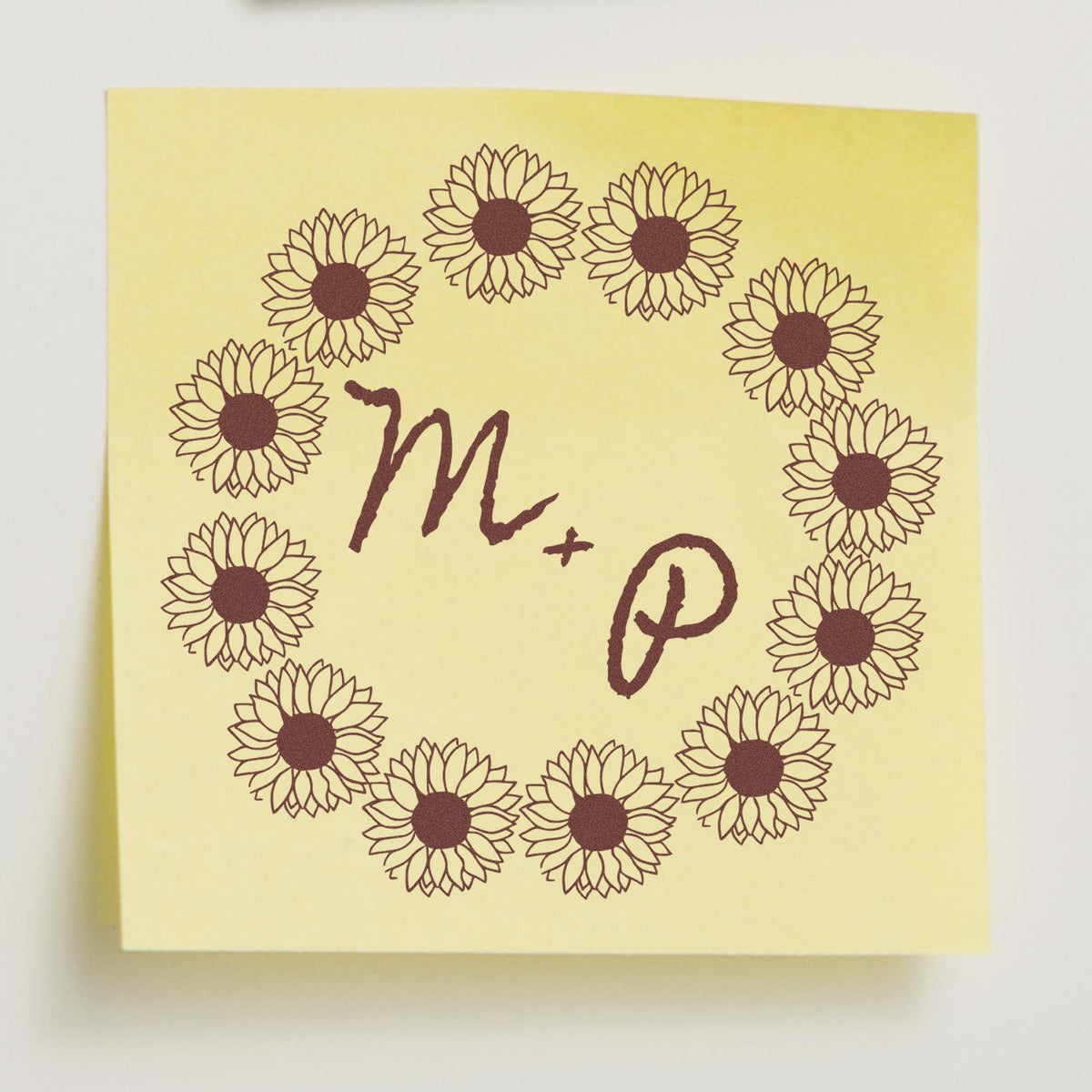 Yellow square stamp seal with brown sunflower wreath framing handwritten M + P monogram.