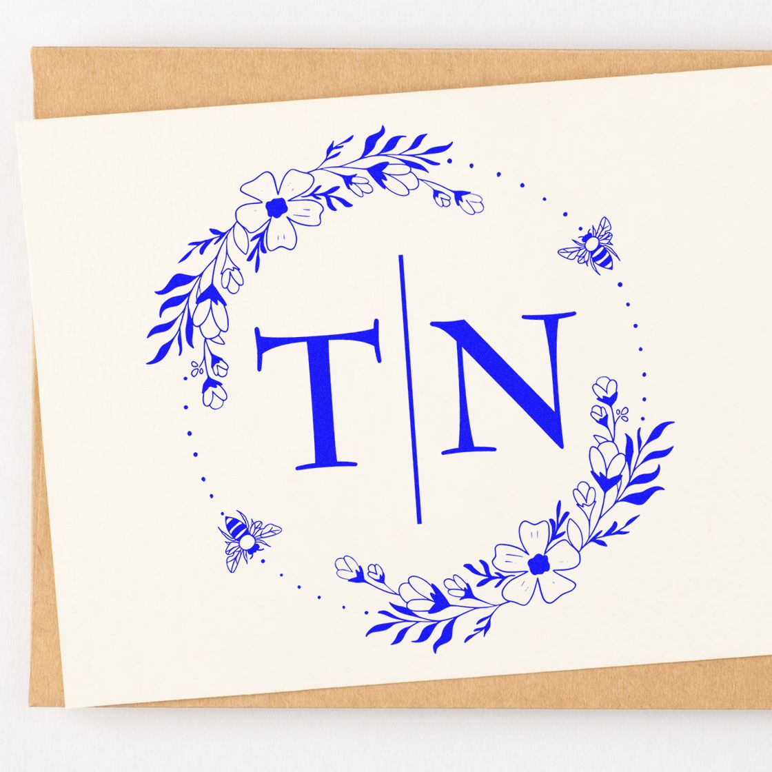 Blue floral TN monogram stamp and seal on white card, with dotted circle, bees, and kraft envelope.