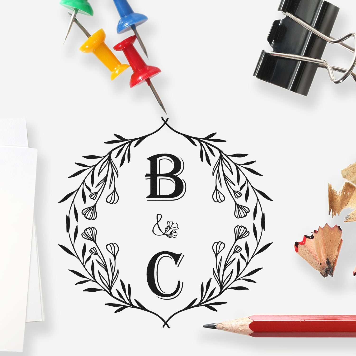 Custom black floral monogram stamp seal with B and C, accented by colorful push pins on a white background.