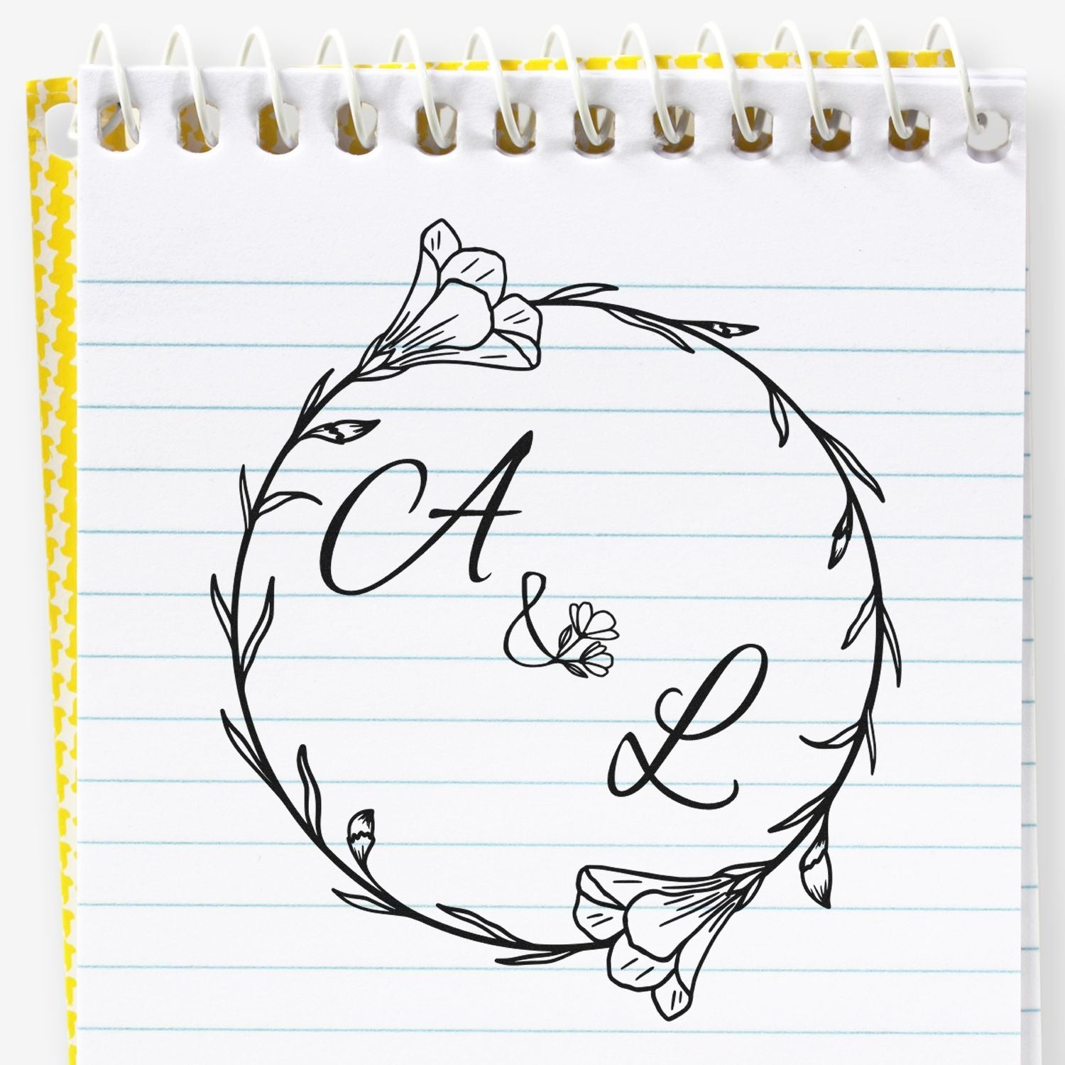 Black floral CA&L stamp seal with wreath on lined notebook paper, yellow border and spiral binding.