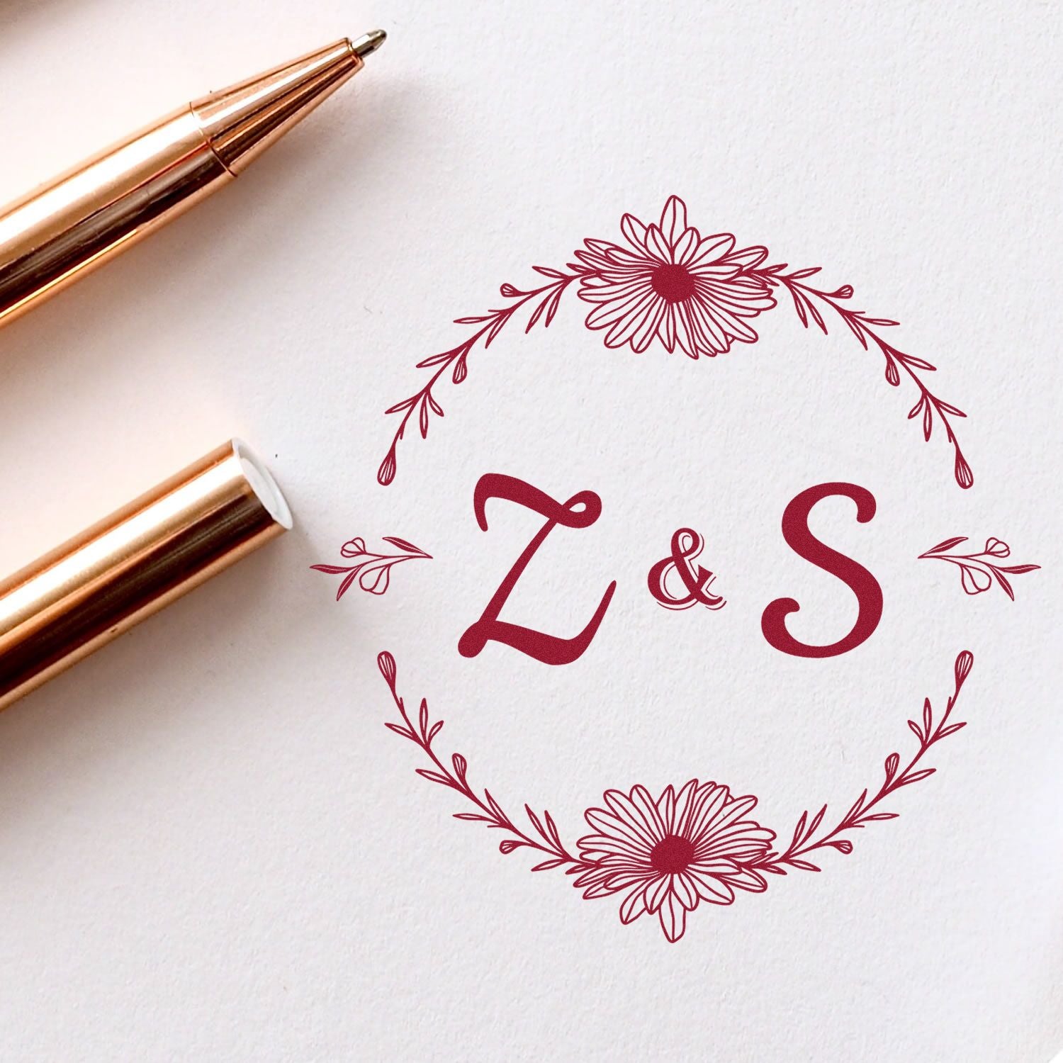 Gold stamp and seal pen beside burgundy floral monogram seal with initials L & S on white paper.