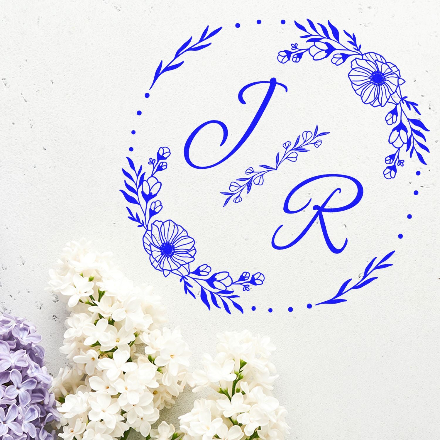 Blue floral monogram stamp and seal with letters C and R on textured white background, accented by white and lilac blossoms.