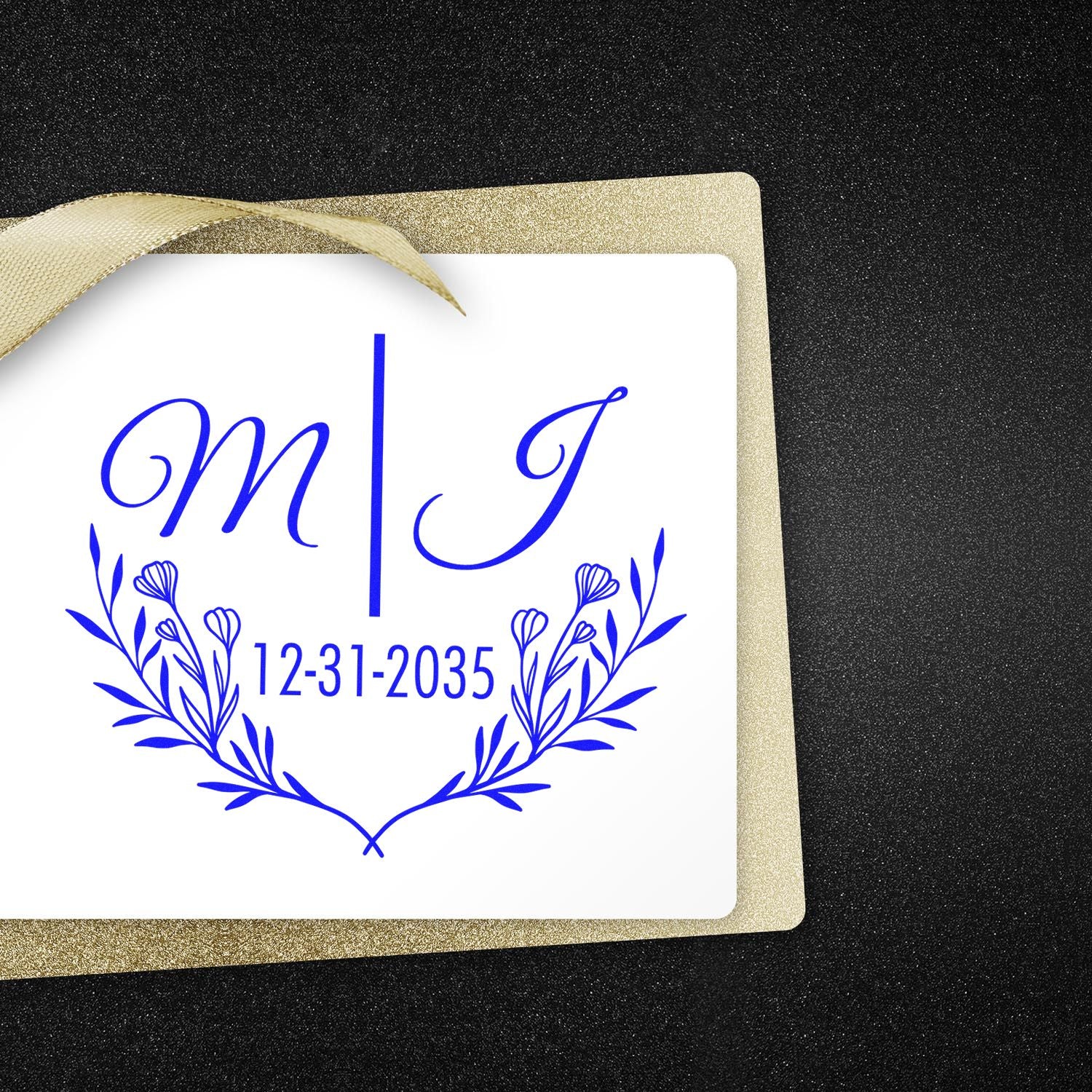 Blue wedding monogram stamp seal with M and J, floral wreath, and 12-31-2035 on white card with gold ribbon.