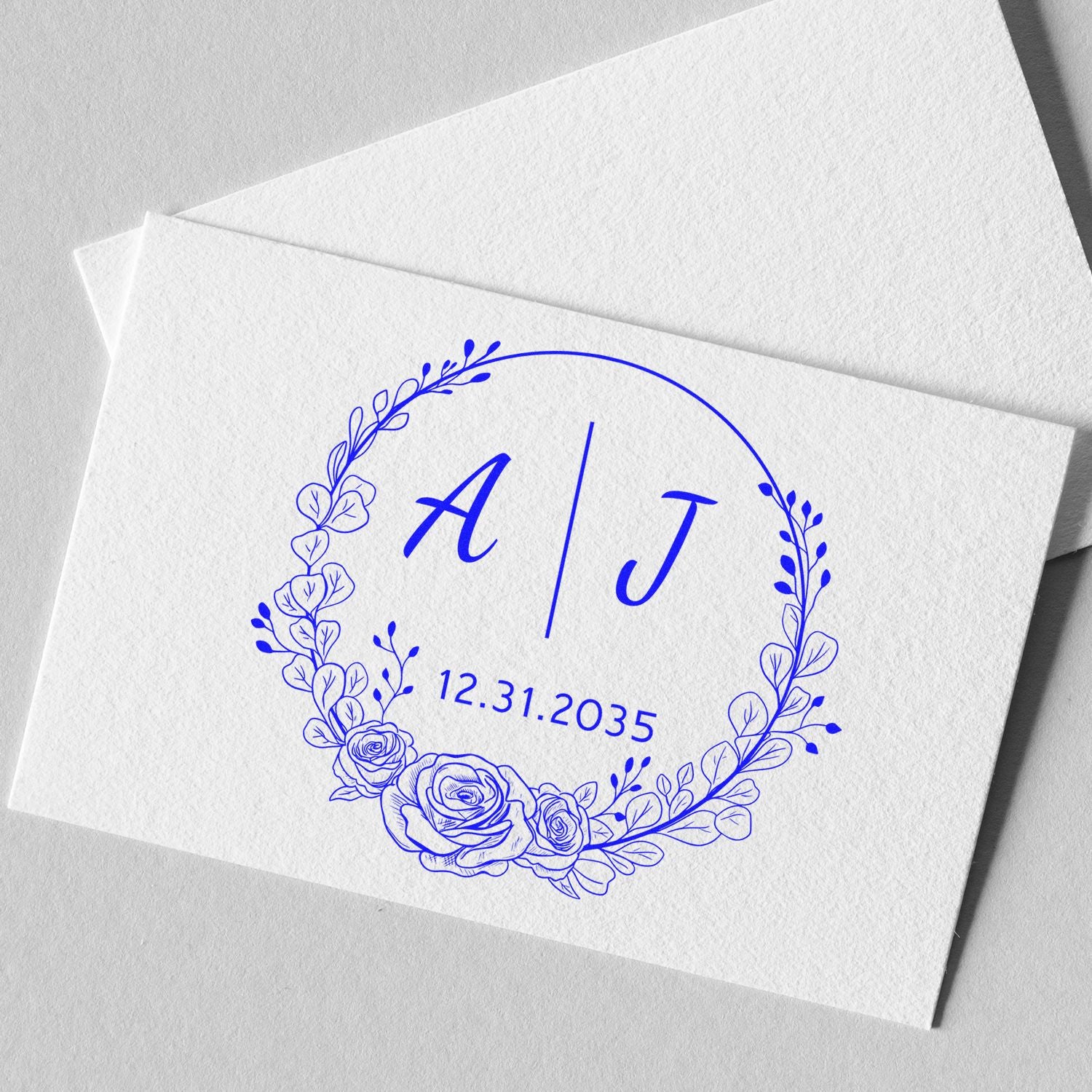 Blue floral wedding stamp seal with initials A | J and date 12.31.2035 on textured white paper.