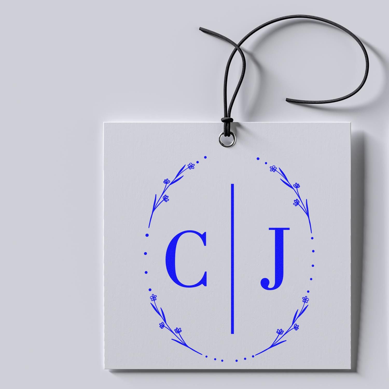 White custom stamp and seal tag with blue floral C|J monogram and black cord on a light gray background
