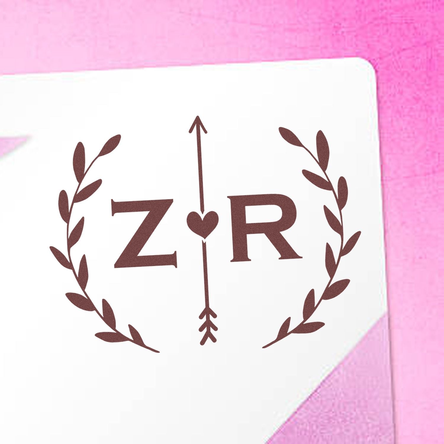 Brown ZR monogram stamp with leafy wreath and heart arrow on a white seal card against a pink background.