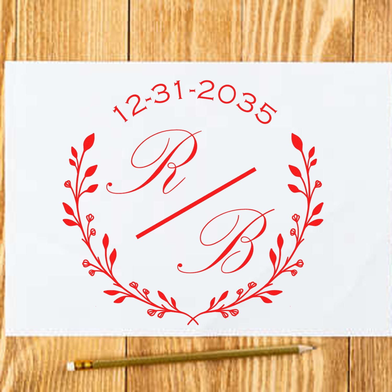 Red custom monogram stamp seal with laurel wreath and date 12-31-2035 on white paper, on a wood table.