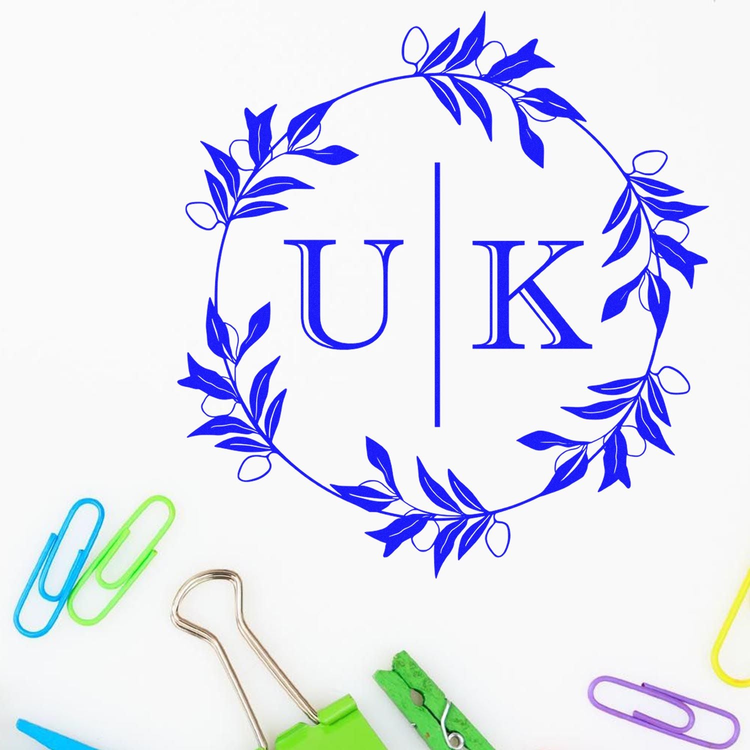 Blue floral wreath stamp and seal design with UK monogram on white, accented by colorful paper clips.