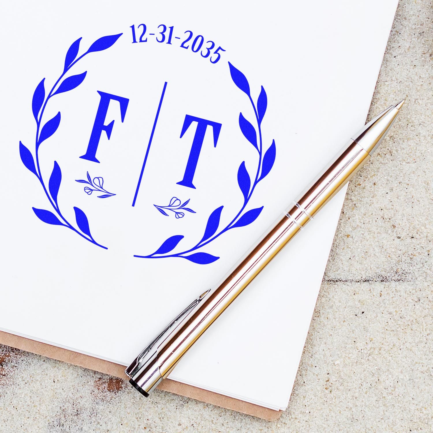 Blue custom stamp seal with laurel wreath, F/T initials, and 12-31-2035 date on white paper beside a gold pen.