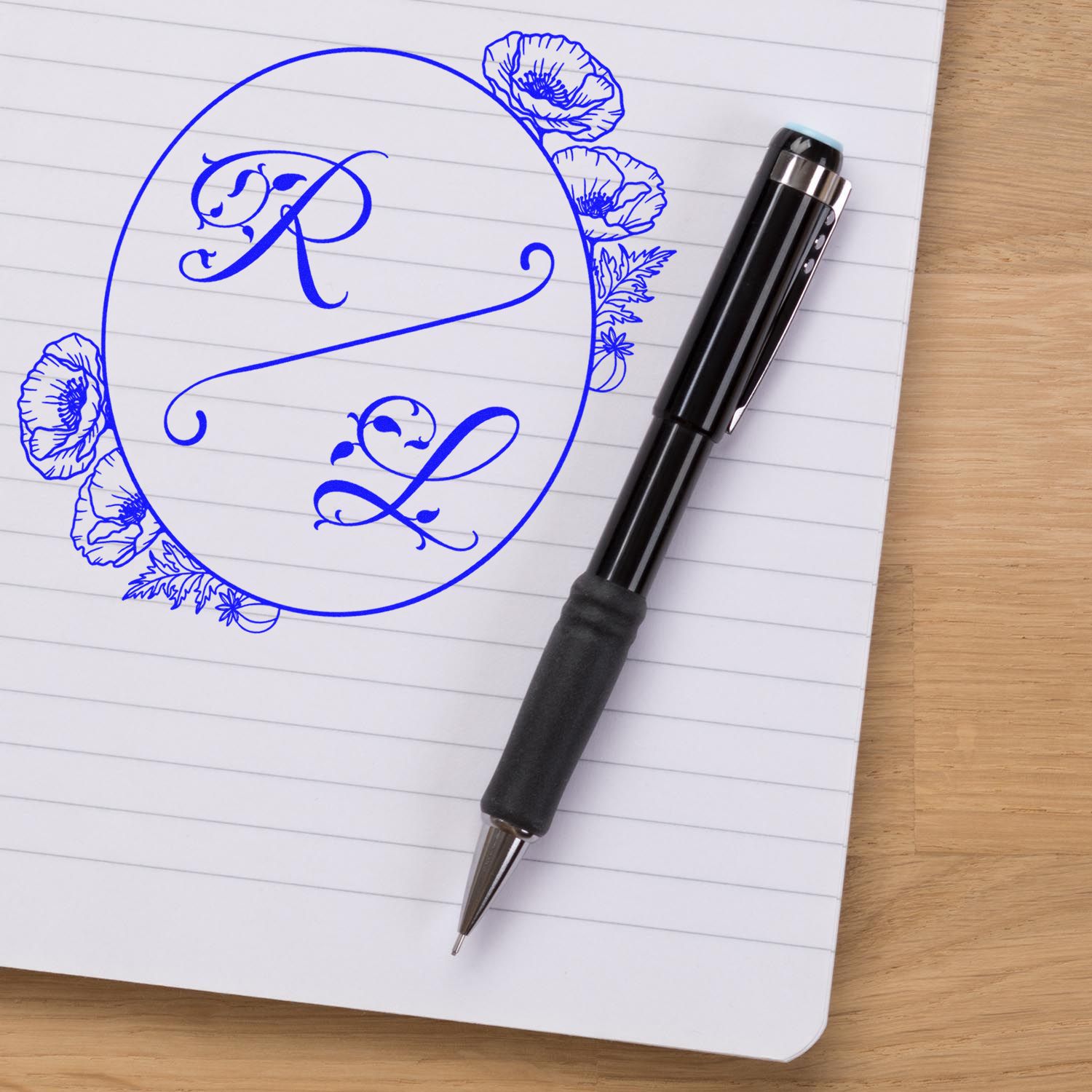 Custom blue monogram stamp and floral seal design on lined notebook beside black pen