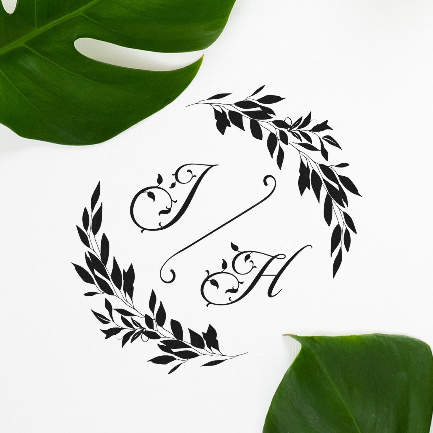 Black monogram stamp and seal with floral wreath and initials on a white background, framed by green leaves.