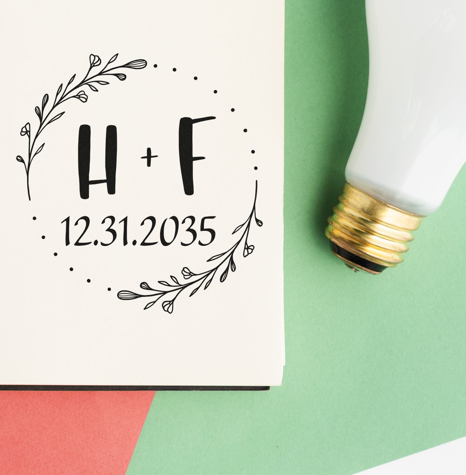 Custom stamp and seal with black floral wreath, H + F, and 12.31.2035 beside a white-and-gold handle on green paper.