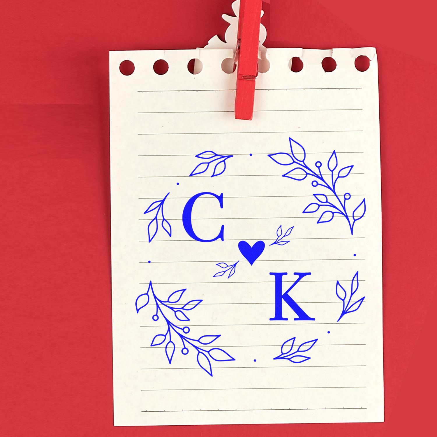 Custom stamp and seal with blue floral C?K monogram on white lined card, clipped with red clothespin on red background