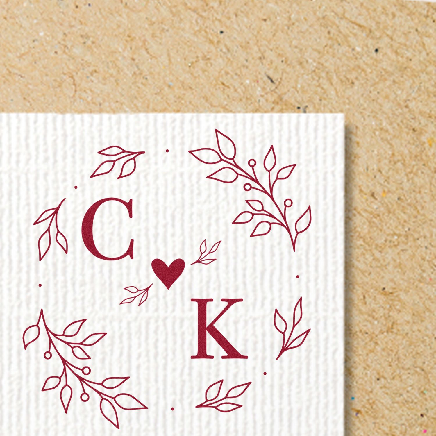 Burgundy C and K monogram stamp and seal with heart and leafy wreath on white textured card.