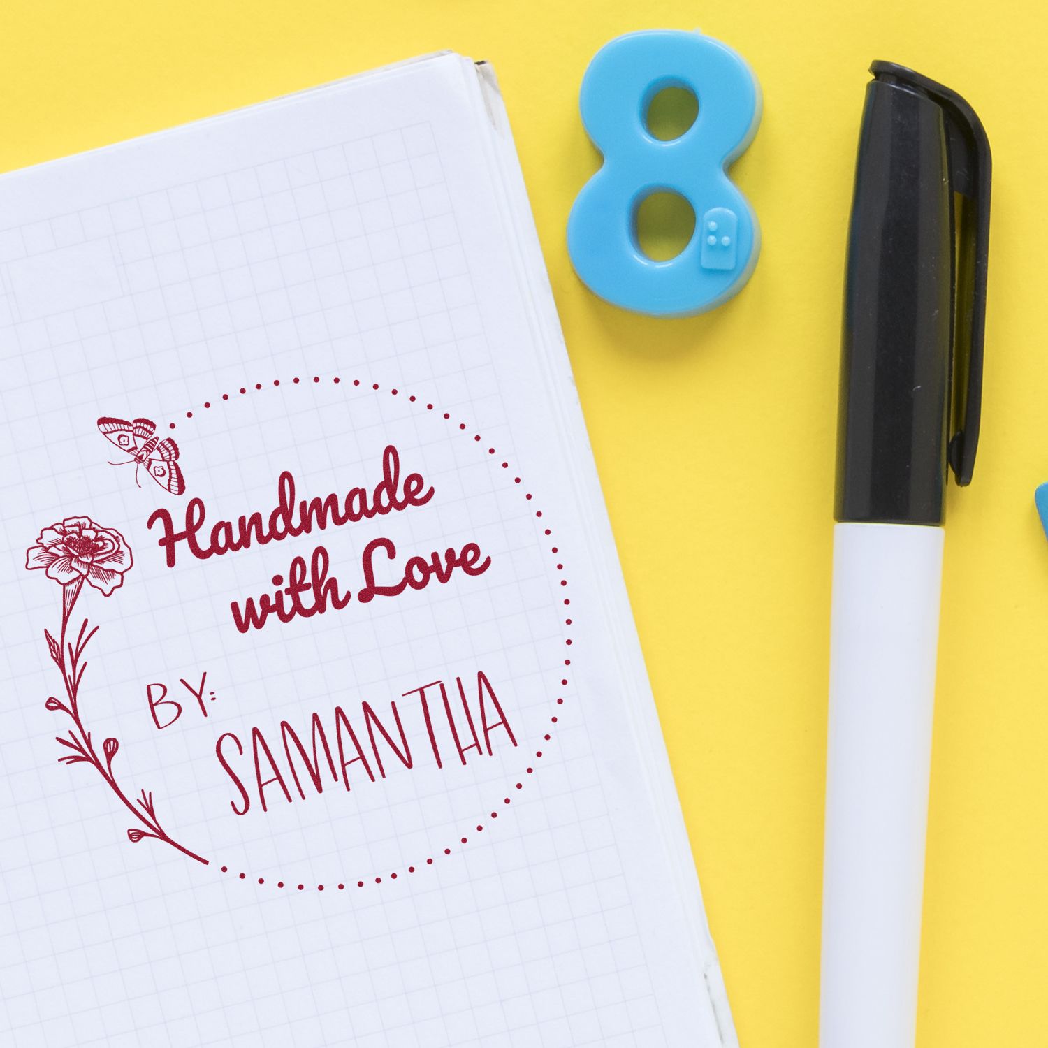 Red handmade stamp on grid notebook with blue number 8 seal and black marker on bright yellow background.