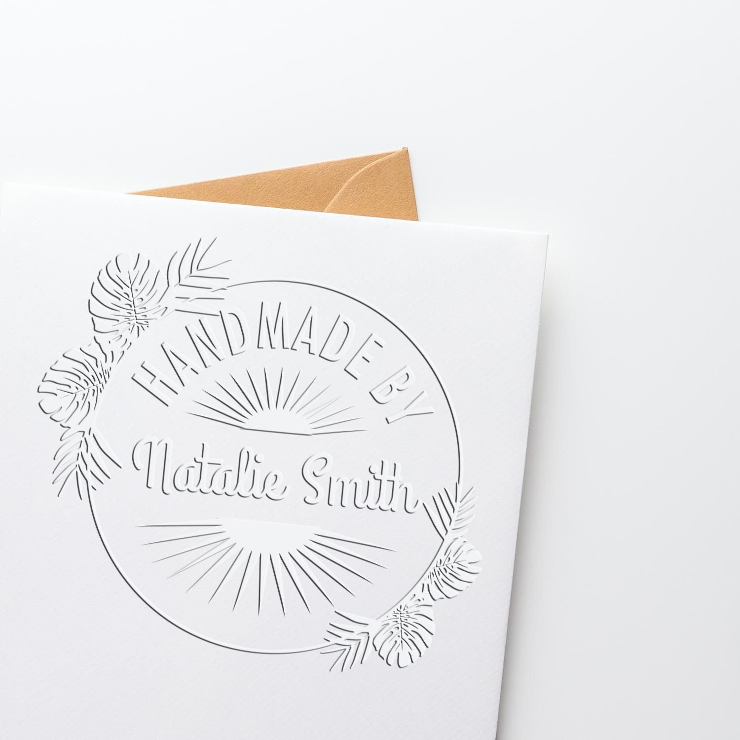 White embossed handmade seal stamp with floral sunburst design on card, shown with a tan envelope.