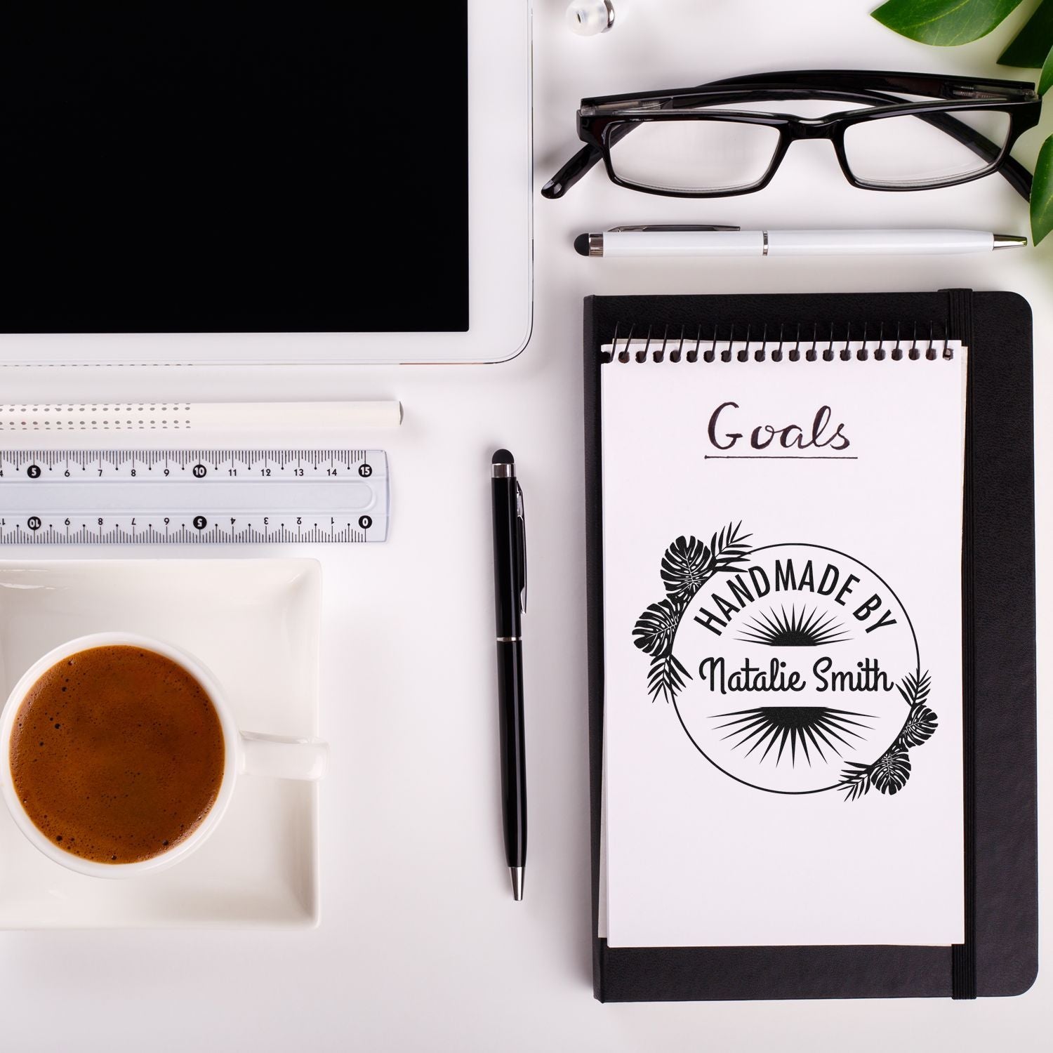 Black notebook with Goals and a handmade by Natalie Smith seal stamp, beside coffee, ruler, pens, and glasses.