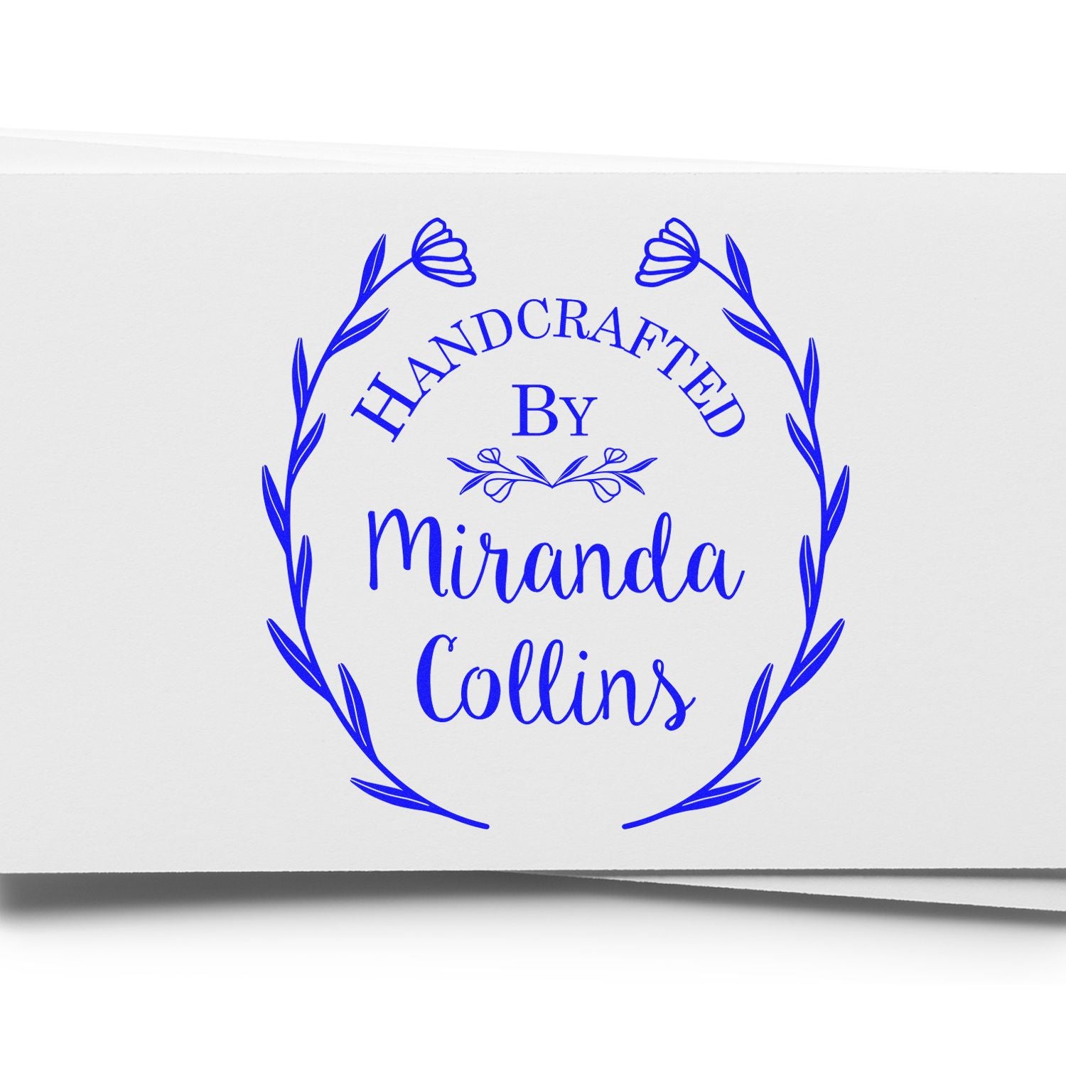 Blue handcrafted seal stamp with floral wreath and text Handcrafted by Miranda Collins in bright blue on white paper.