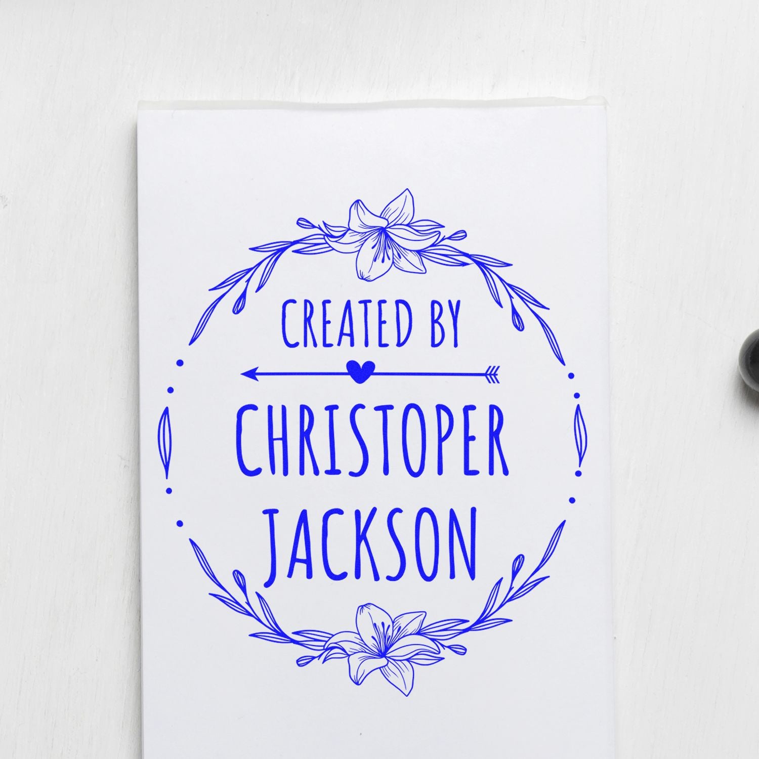 Blue custom stamp seal with floral wreath, heart arrow, and Created by Christopher Jackson on white paper.
