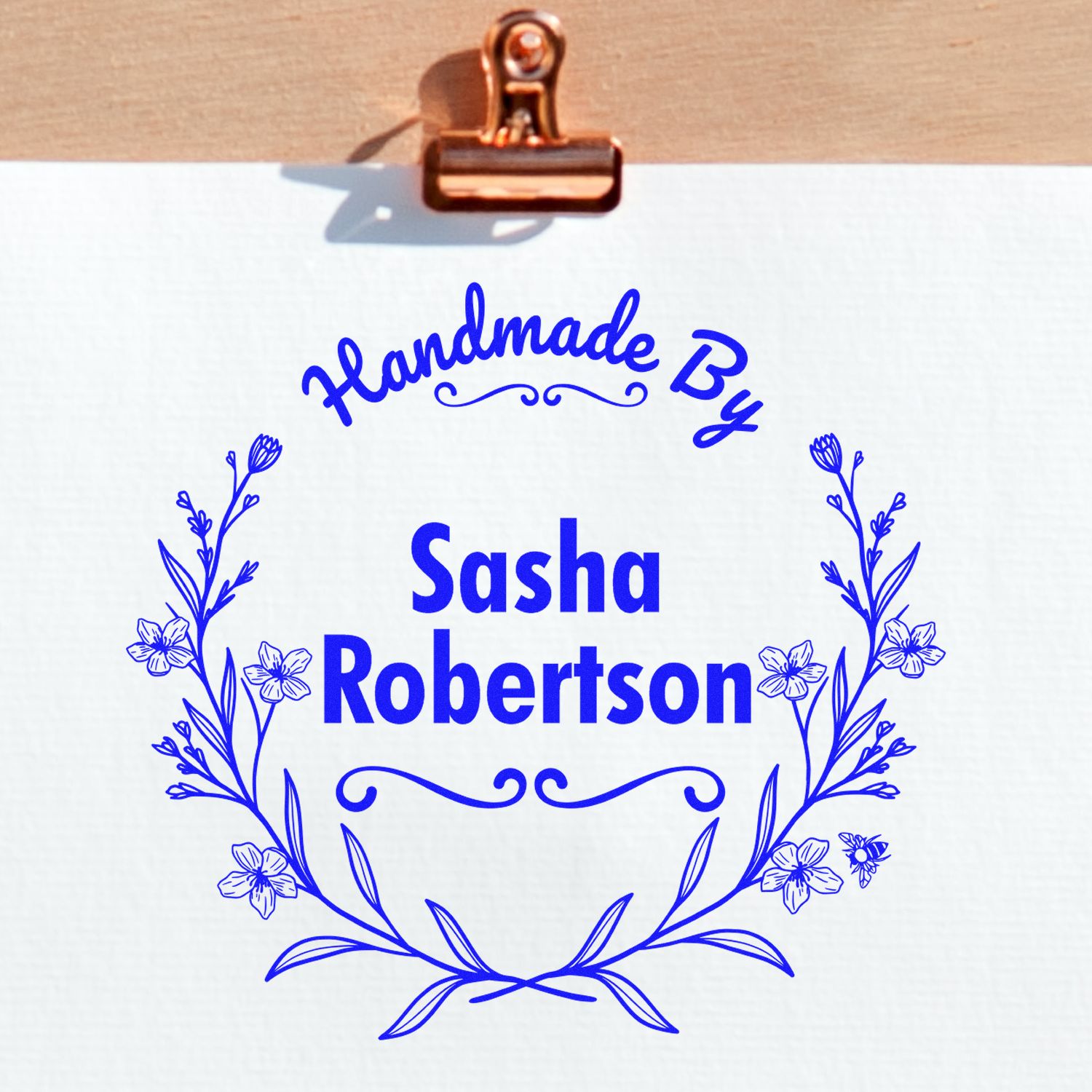 Copper clip holding white sheet with blue floral handmade stamp seal reading Sasha Robertson