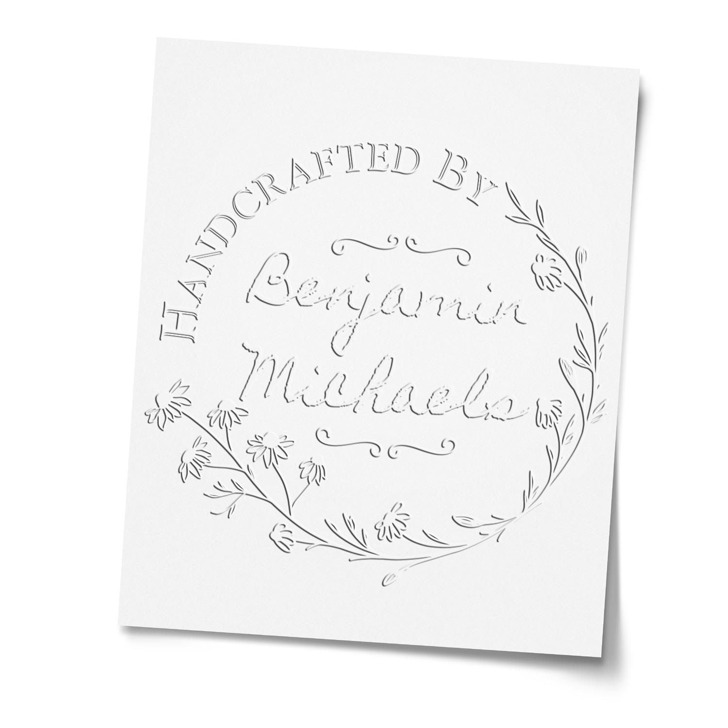 White embossed custom stamp seal with floral wreath border and cursive Benjamin Michael text on a clean card.