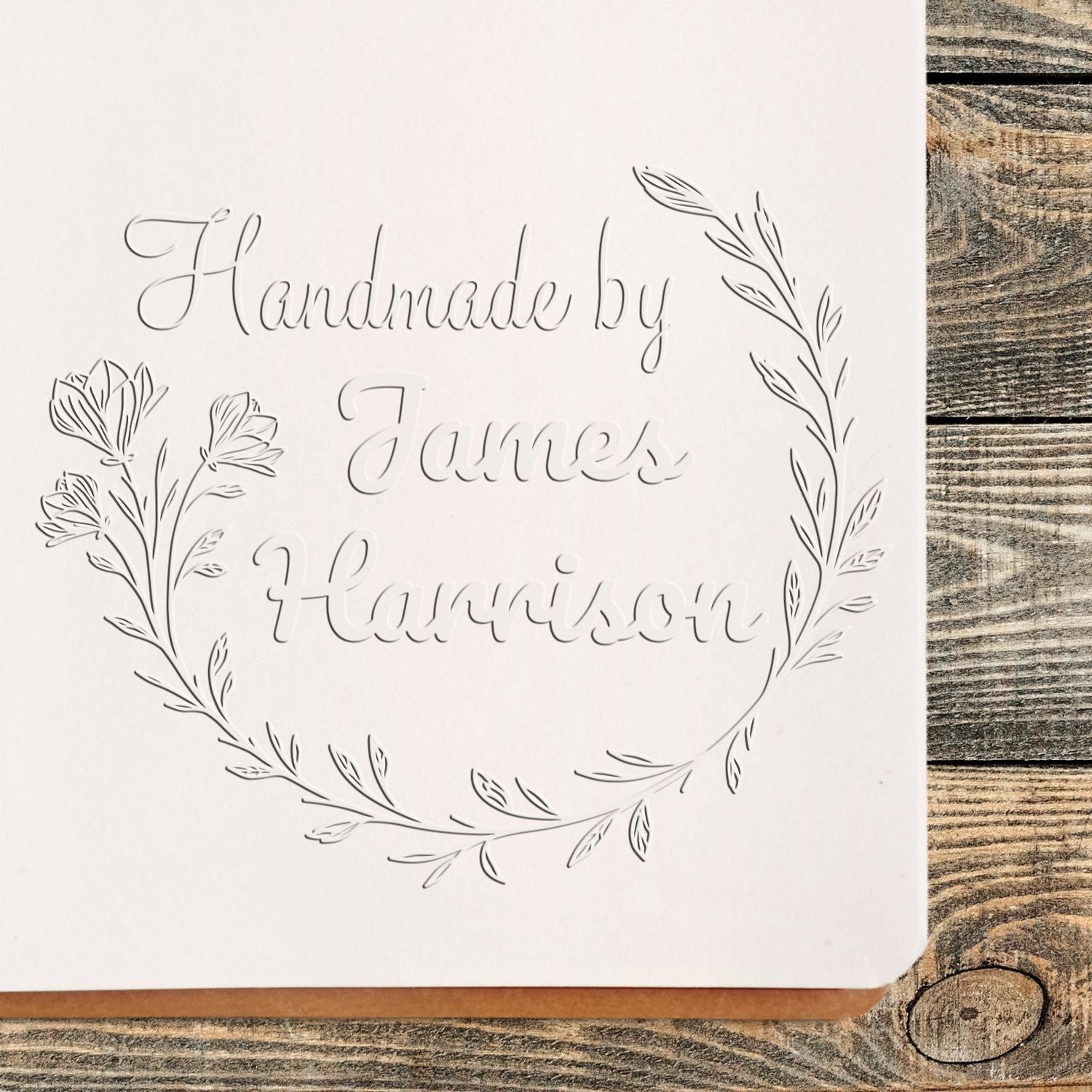 Custom embossing stamp seal with gray floral wreath and handwritten text Handmade by James Harrison on white card.