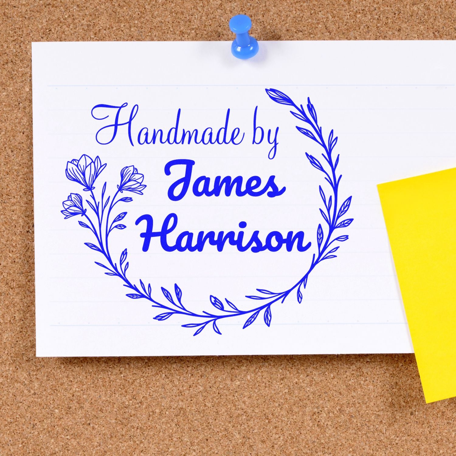 Blue handmade stamp and seal reading Handmade by James Harrison with floral wreath on white card, pinned to corkboard.