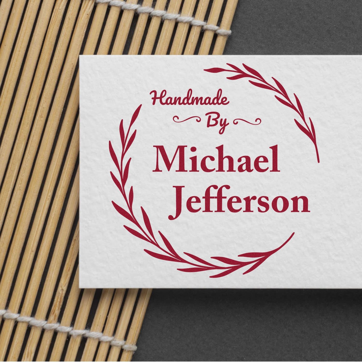 Red handmade stamp seal reading Michael Jefferson with laurel wreath design on white paper over bamboo mat