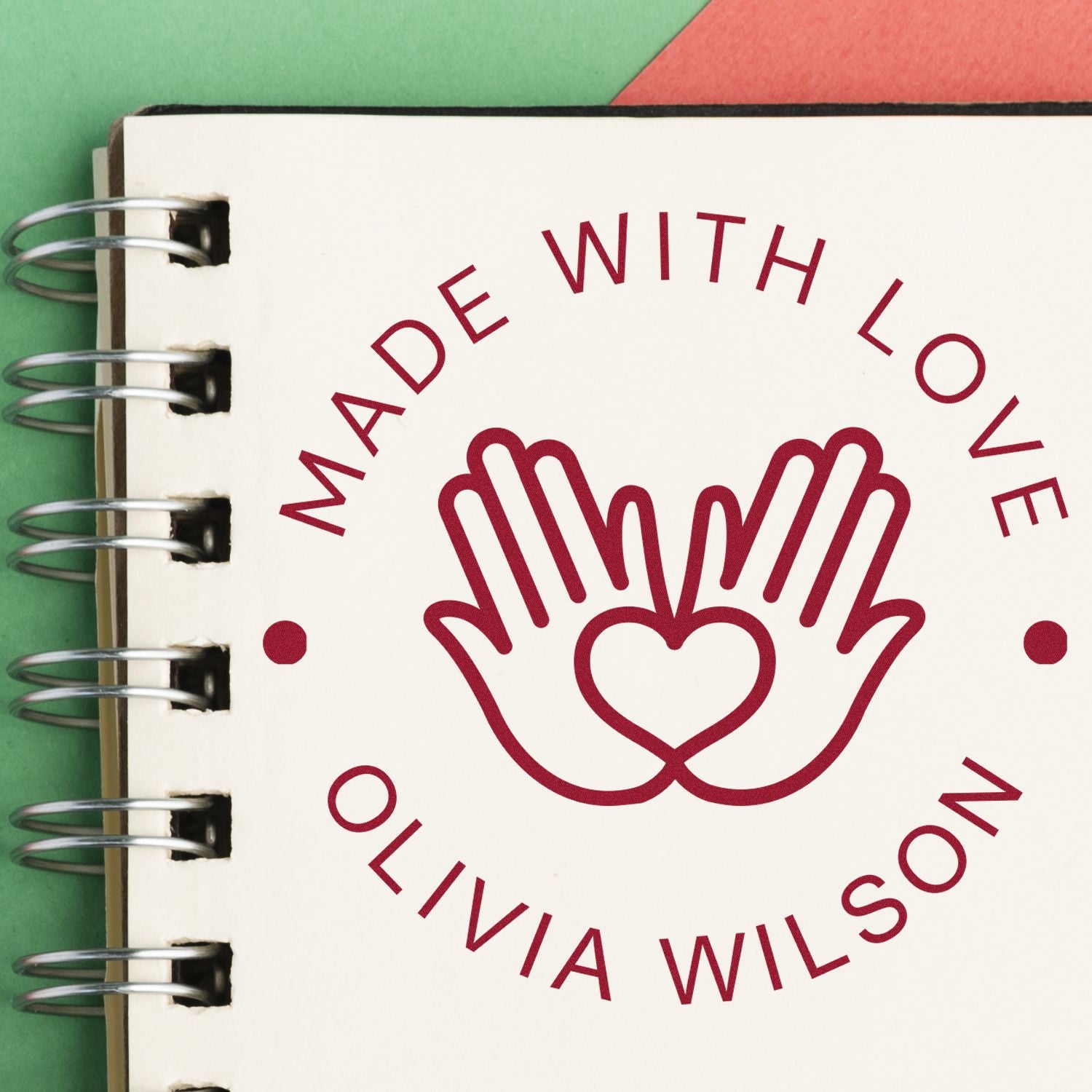 Burgundy Made with Love stamp and seal on white spiral notebook page, with heart and hands logo on green and red background.