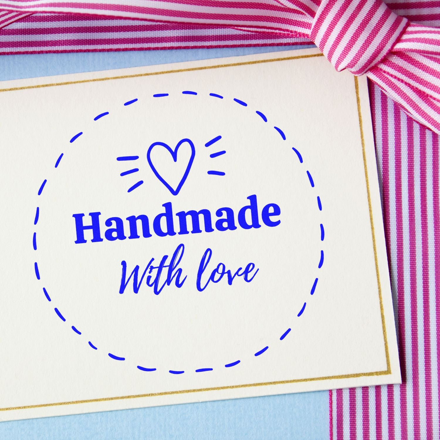 Blue handmade with love stamp seal on white card, framed by a gold border and pink striped ribbon.