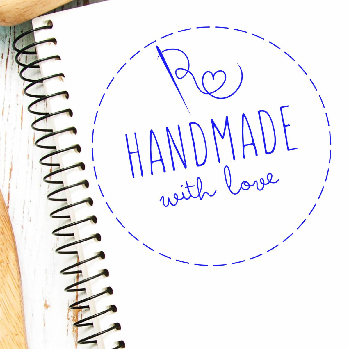 Blue handmade with love stamp seal in a dashed circle on a white spiral notebook, with a heart monogram.