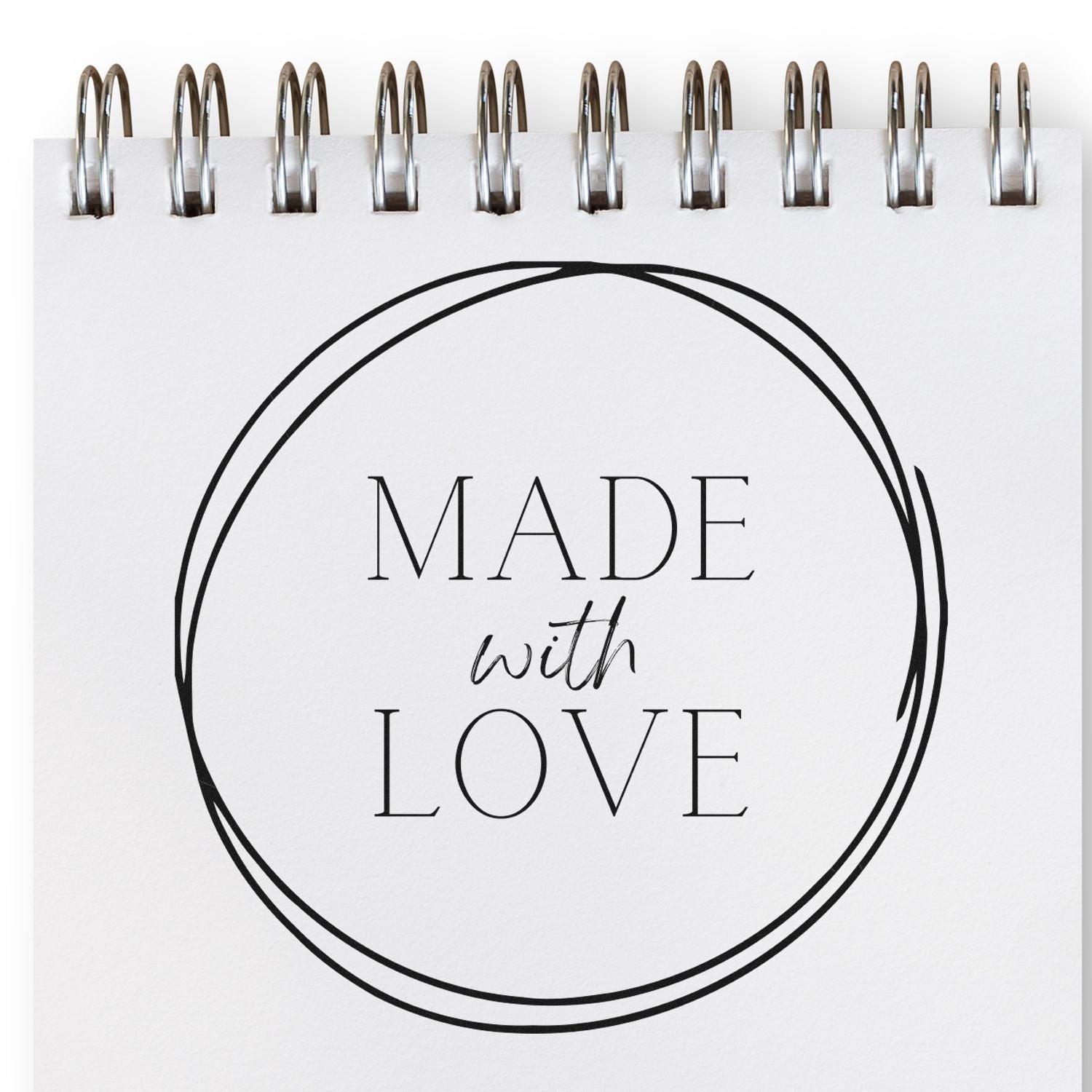 Black circular stamp seal with Made with Love on a white spiral-bound notepad, silver rings at top.
