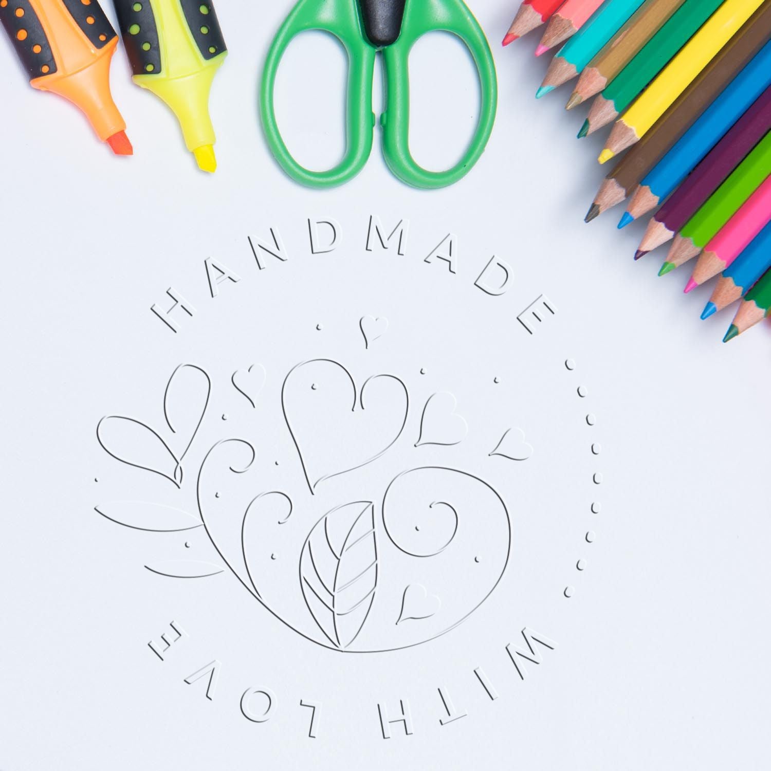 Colorful stamp and seal products with pencils and scissors around an embossed Handmade with love heart design on white paper.