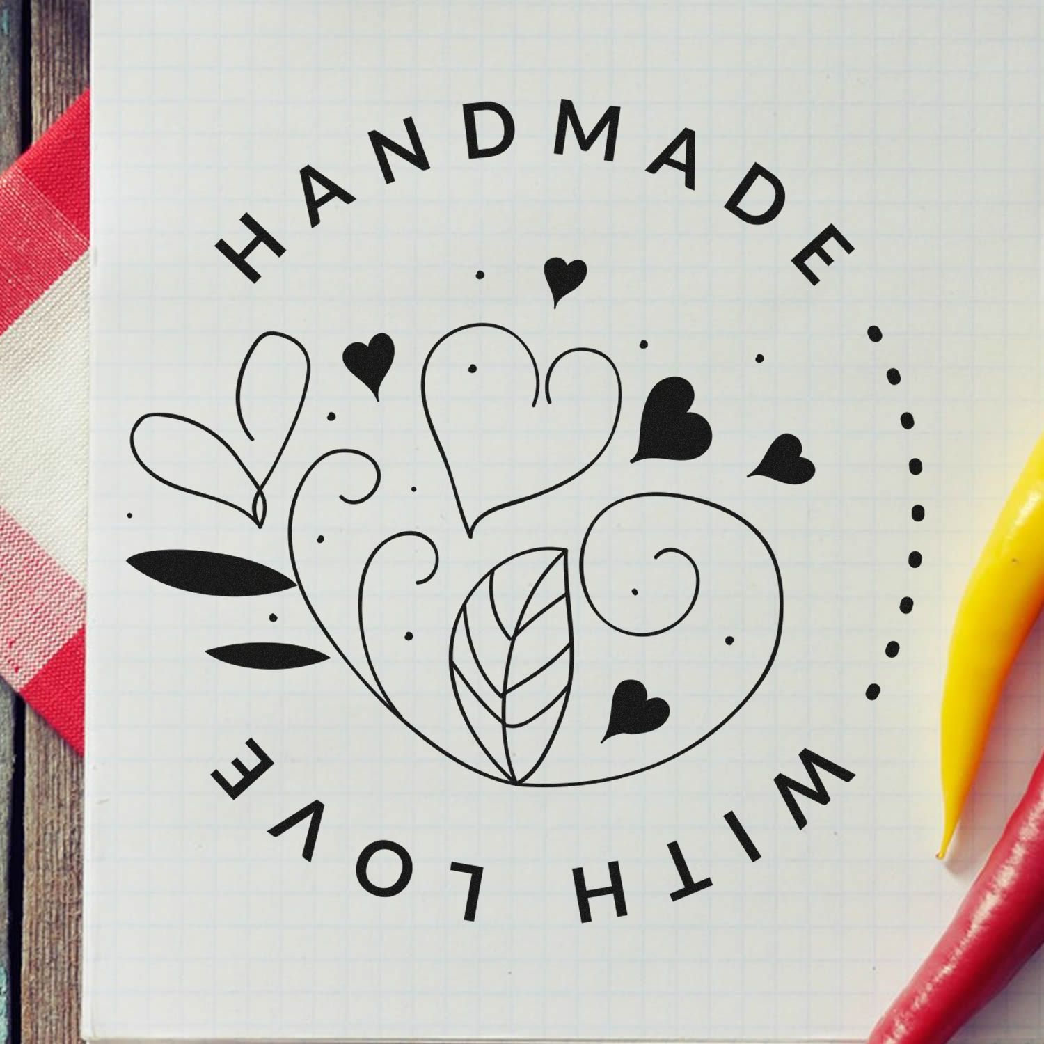 Black handmade stamp and seal design with hearts, swirls and leaves on white grid paper.