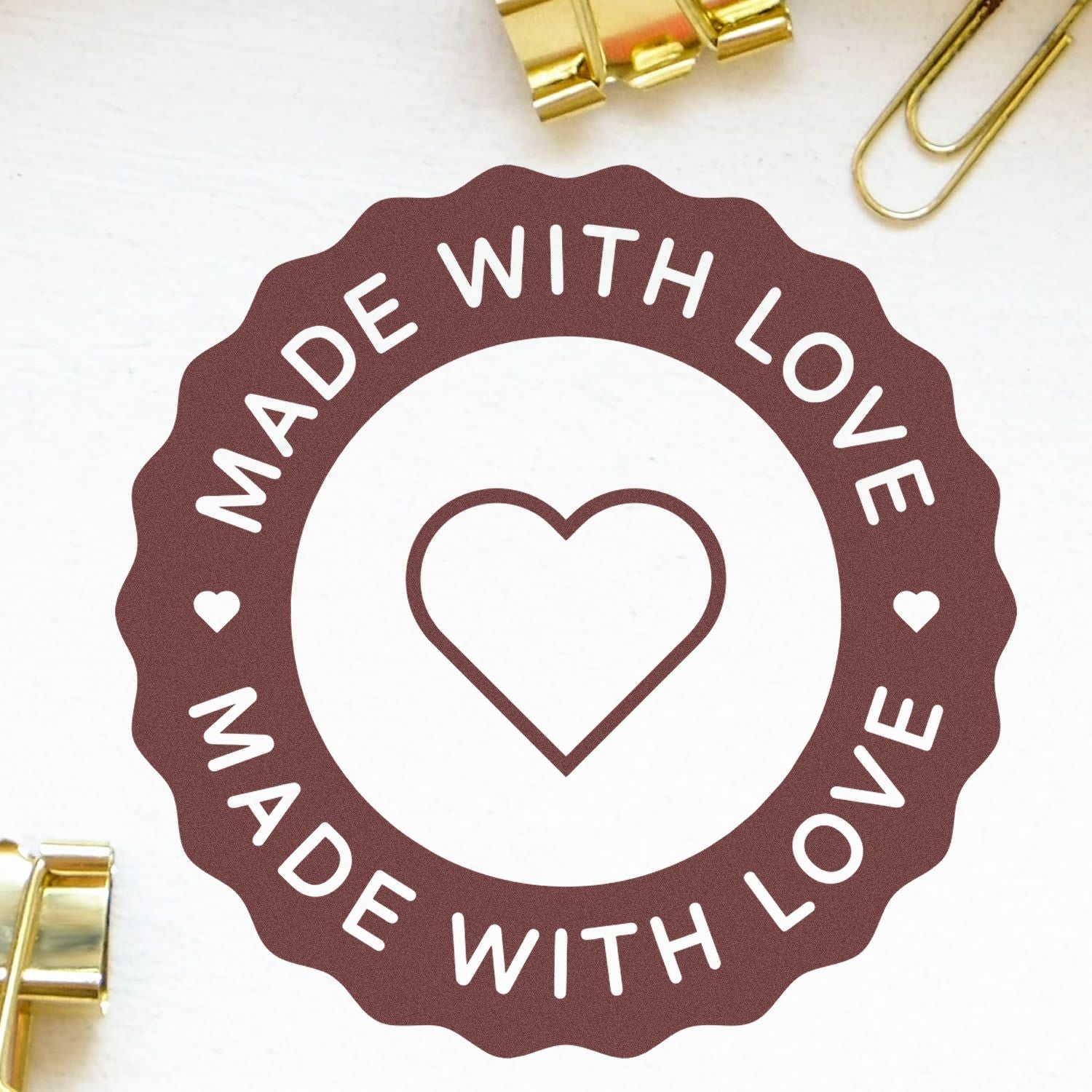 Brown scalloped stamp seal with white Made with Love text and heart, shown on a white background with gold clips.