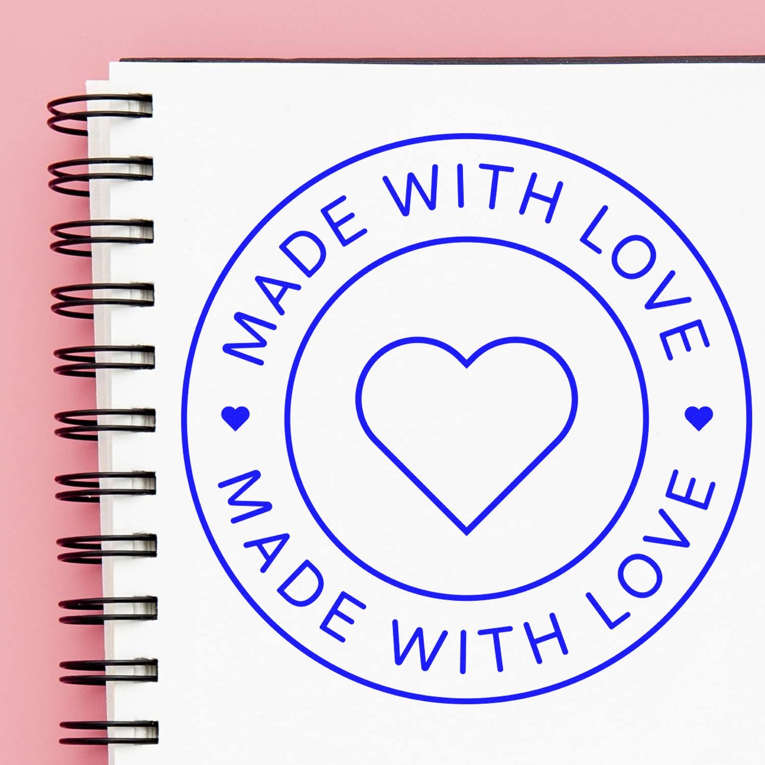 Blue Made with Love heart stamp seal on white spiral notebook, with pink background.