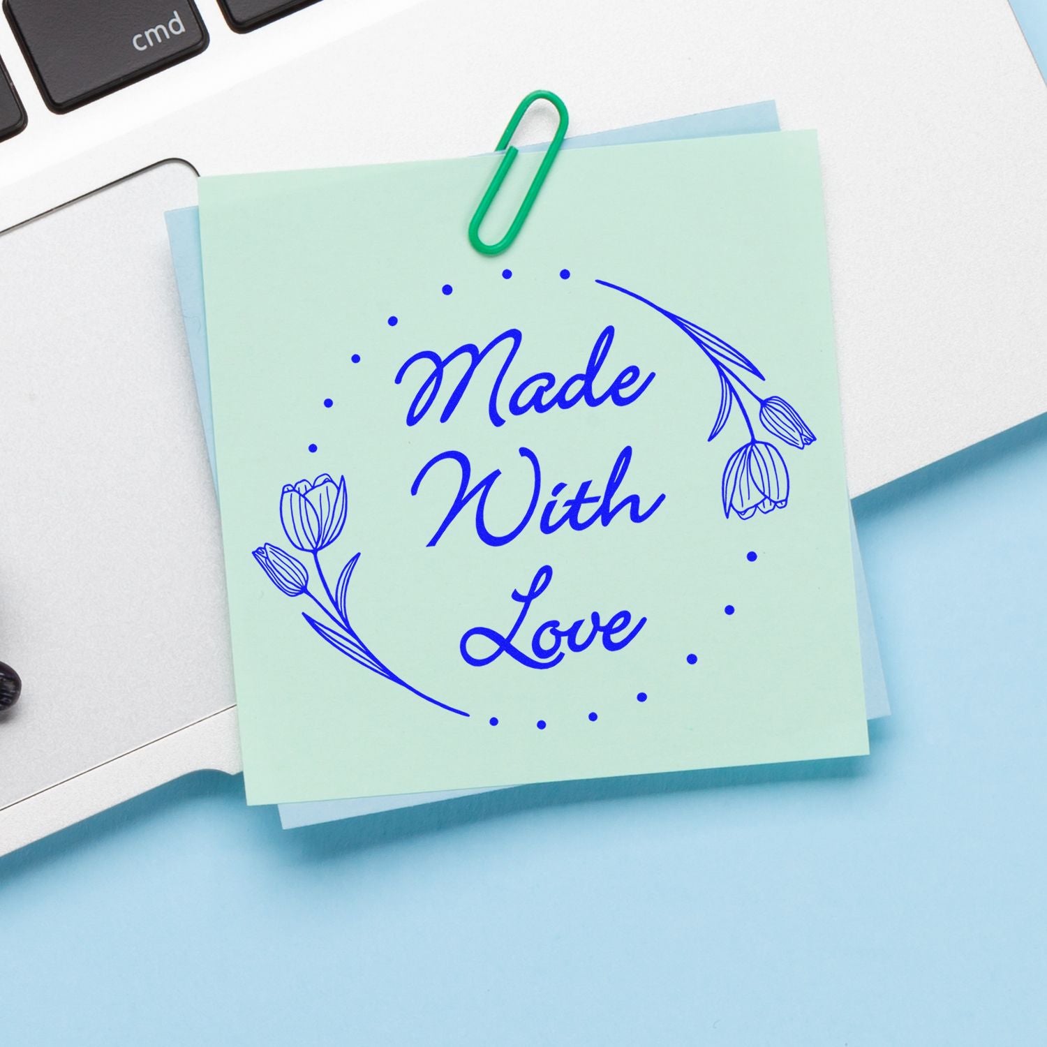 Mint green stamp and seal sample with blue “Made With Love” script, floral accents, and a green paperclip on a white desk.