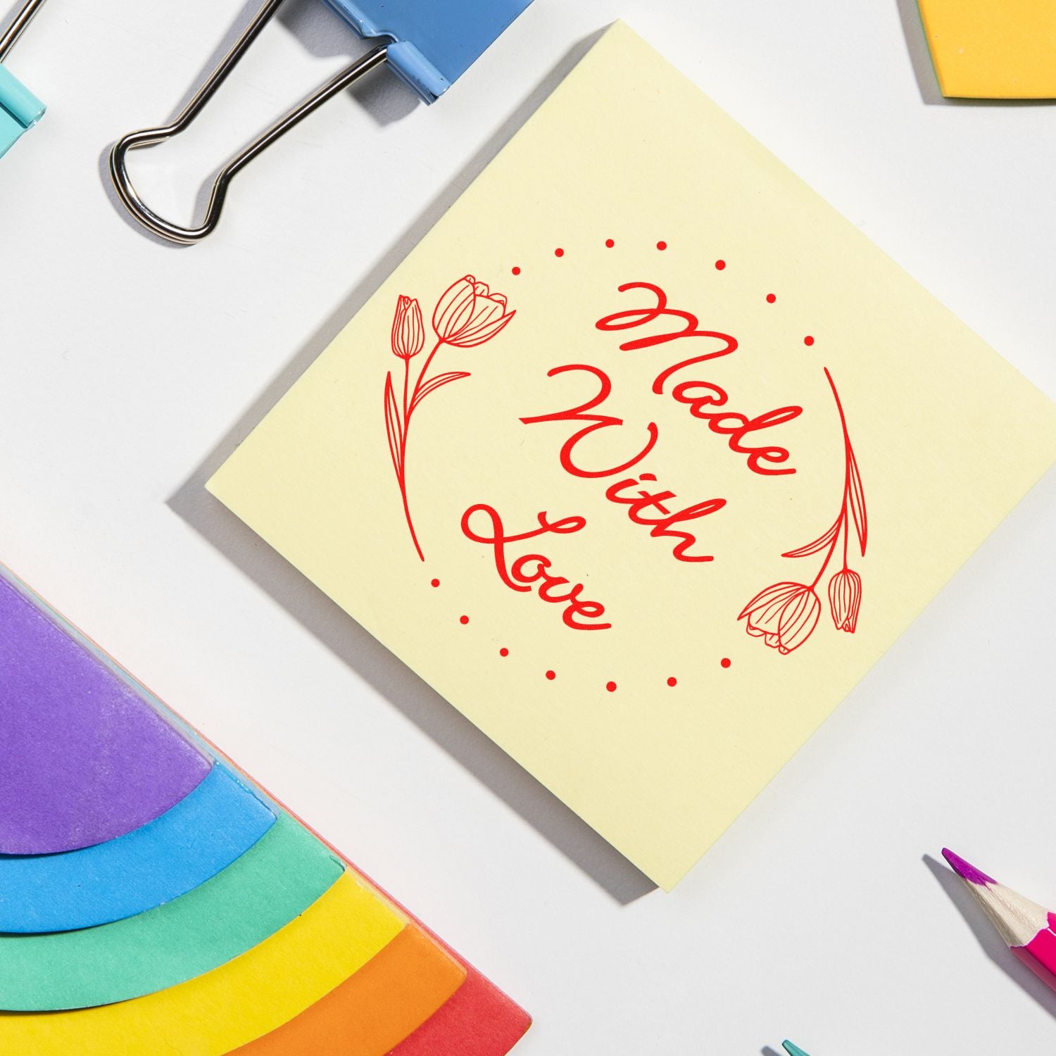 Yellow sticky note with red “Made With Love” floral stamp, surrounded by colorful seal tabs, binder clips, and a pencil.