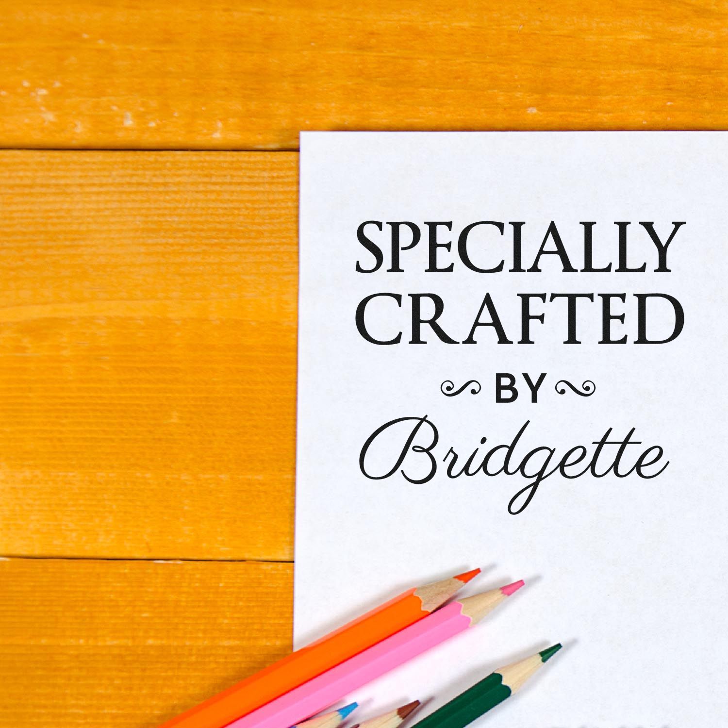 Custom stamp and seal design reading Specially Crafted by Bridgette on white paper with colored pencils on a yellow wood background.